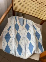 Chaleco de punto con diseño de rombos en tonos crema y azul, cuello en V y terminaciones acanaladas.