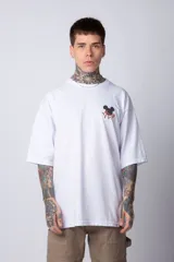 Remera blanca de corte oversize confeccionada en algodón pesado, con cuello redondo y mangas cortas. Presenta un pequeño estampado frontal con la silueta de Mickey Mouse y caracteres orientales, y un diseño gráfico de mayor tamaño en la espalda.