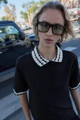 Top de tejido negro con cuello polo y bordes de manga cortos con diseño de ondas en blanco y negro. Tiene un cierre frontal de botones.