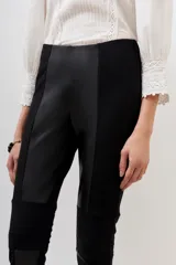 Pantalon negro de corte ajustado, confeccionado en una combinación de materiales que incluye paneles de efecto cuero en la parte frontal y laterales, con diseño de costuras horizontales en las rodillas.