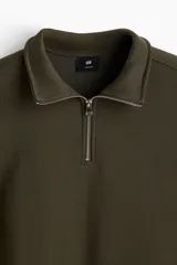 Buzo de tejido pesado de mezcla de algodón con interior cepillado suave, color verde oliva. Modelo con hombros caídos, cuello elevado con medio cierre metálico y puños y bajo en punto acanalado.