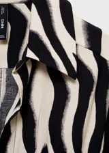 Vestido camisero midi de tejido fluido con estampado de cebra. Presenta cuello camisero, cierre frontal de botones, mangas cortas y lazo ajustable en la cintura para entallar la silueta.
