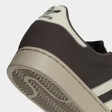 Championes Adidas Superstar II de cuero nobuk en color marrón oscuro, con las icónicas tres rayas laterales y la puntera de caucho en tono crema. Presenta una suela de caucho al tono y forro interior de felpa.