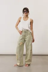 Pantalón de jean de corte wide leg, tiro medio y lavado claro con efecto desgastado. Presenta diseño de múltiples paneles con costuras pespunteadas verticales y roturas en ambas piernas.