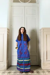 Vestido largo verde militar de popelina de algodón, con diseño oversized, cuello mao, mangas cortas, bolsillos laterales y cierre frontal con botones. Presenta un estampado de flores grandes en la parte superior y franjas horizontales de colores en el ruedo.