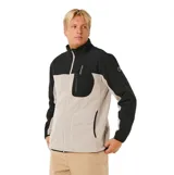 Canguro con cierre frontal de la línea Anti Series de Rip Curl. Presenta un diseño de bloques de color en beige y negro, cuello alto, bolsillos laterales y un bolsillo vertical con cierre en el pecho que incluye el logo de la marca.