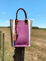 Bolso matero color fucsia con textura croco, laterales color beige con borde blanco y manijas de cuero marrón.