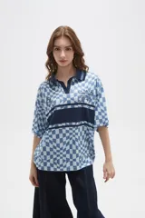 Remera tipo chomba de manga corta con cuello camisero, confeccionada en tejido con estampado de tablero ondulado en tonos rosado y blanco, con franja horizontal y detalles gráficos en color bordó.