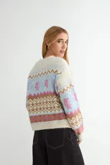 Cardigan de punto con diseño jacquard multicolor, cuello redondo y cierre frontal con botones. Presenta un patrón geométrico y floral en tonos verde, rojo, azul y crema.
