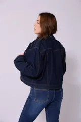 Campera de jean de mujer, color azul claro lavado, con corte cropped y estilo clásico. Presenta cuello camisero, botones metálicos frontales y bolsillos de parche en el pecho.