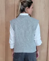 Chaleco de punto gris con diseño de trenzas y rombos en relieve, cuello redondo y terminaciones acanaladas.