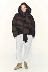 Campera puffer corta de color marrón oscuro, con diseño acolchado, cuello alto y capucha integrada. Presenta cierre frontal con botones magnéticos y mangas largas con puños elásticos.