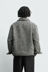 Sobrecamisa de corte relajado con textura de tejido estructurado en color gris y negro. Presenta cuello clásico, cierre frontal con botones, mangas largas con puños abotonados y bolsillos de plastrón en el pecho.