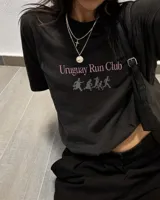 Remera negra de corte regular con estampado frontal que dice "Uruguay Run Club" en color rosado y siluetas grises de personas corriendo debajo.