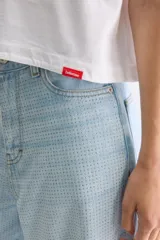 Remera cropped blanca de calce relajado, con cuello redondo, hombros caídos y mangas cortas. Presenta un pequeño detalle de etiqueta bordada en el lateral inferior.
