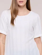 Blusa blanca de tejido de punto liviano con textura labrada en franjas verticales y caladas, de silueta evasé, con escote redondo, manga corta y ruedo asimétrico en picos.