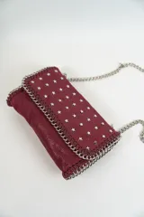 Cartera de hombro color azul marino, con solapa frontal decorada con tachas en forma de estrellas plateadas. Los bordes están adornados con un detalle de cadena entrelazada y la correa es una combinación de cadena plateada y una sección de cuero sintético.