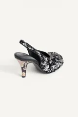 Zapato de tacón destalonado con abalorios y lentejuelas en tonos negros y plateados, escote redondo, punta redonda y tacón fino alto.