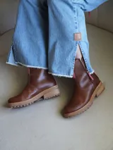 Botas cortas de cuero blanco con suela track marrón y detalles en gamuza beige en la parte frontal y trasera. Cuenta con cierre lateral y tirador de cuero.