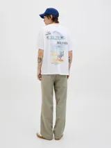 Remera de corte holgado color blanco, con cuello redondo y manga corta. Presenta una estampa artística en la espalda con motivos de playa, sombrilla y silla de descanso.