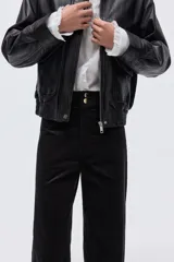 Pantalón de pana de algodón color negro, de tiro alto, con pliegues delanteros y traseros. Cierre con dos botones dorados, bolsillos traseros abiertos y piernas rectas.