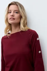 Sweatshirt color bordó con cuello redondo y mangas tres cuartos. Presenta detalles de botones metálicos decorativos a lo largo de los hombros y las mangas.
