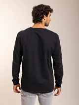 Remera blanca de manga larga con cuello redondo y logo bordado de un pájaro en el pecho.
