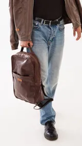 Mochila de cuero genuino color marrón, con diseño minimalista, compartimento principal con cierre, bolsillo frontal con etiqueta de marca y correas ajustables.