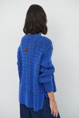 Buzo reversible de tejido de punto con diseño de trenzas, cuello redondo y mangas largas. Presenta una combinación de colores en contraste, con un lado en violeta y el otro en marrón oscuro.