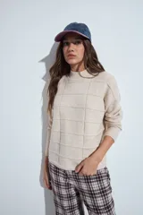 Sweater de punto gris con cuello a la base y diseño de trama geométrica en relieve. Presenta un calce relajado con mangas largas y puños tejidos.