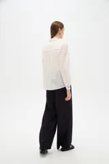 Camisa de algodón blanca de corte holgado, con cuello camisero, mangas largas y bordados florales multicolores. Presenta detalles de calados en los hombros y cierre frontal con botones.