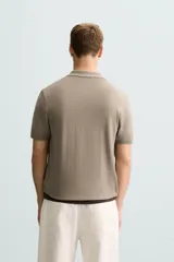 Polo de punto negro, manga corta, con cuello solapa y cierre frontal de tres botones. Presenta un calce regular y acabados en rib en mangas y ruedo.