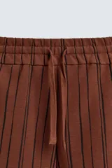 Bermuda de corte relajado color marrón con finas rayas verticales negras. Presenta cintura elástica ajustable con cordón y bolsillos laterales y trasero.
