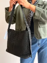 Bolso tipo hobo con estampado animal print en tonos negros, confeccionado en material sintético. Cuenta con una correa larga regulable, cierre superior y un mini monedero desmontable a juego.