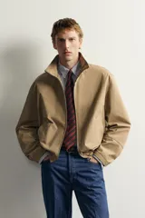Cazadora regular fit de la colección Aaron Levine x ZARA, confeccionada en tejido con mezcla de algodón con patrón de cuadros pequeños en tonos beige y marrón. Cuenta con cuello subido, manga larga con puño ajustable con botón a presión, bolsillos de vivo en la cadera, bajo ajustable con elástico en los laterales y cierre frontal con cremallera.