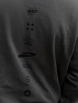 Buzo oversize de cuello redondo en color gris, con diseño estampado en el frente que incluye logotipos y texto. Presenta puños y ruedo acanalados, con una pequeña etiqueta decorativa en la parte inferior.