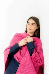 Ruana tejida color fucsia con flecos en el borde inferior.