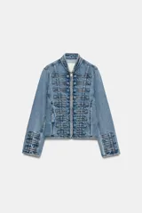 Chaqueta denim entallada de cuello redondo y manga larga, con cierre frontal de cremallera metálica. Presenta detalles de aplicaciones en el mismo tejido y pasamanería frontal de inspiración militar.