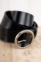 Cinto de cuero negro, ancho, con hebilla metálica plateada de forma ovalada o redonda.