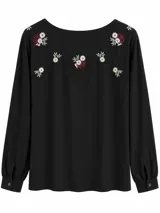 Blusa negra de manga larga con cuello redondo y delicados bordados florales en la parte superior delantera y en los hombros. Cuenta con puños abotonados.