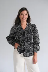 Blusa de manga larga con cuello mao y cierre frontal de botones. Presenta un diseño estampado con líneas blancas abstractas sobre fondo negro.