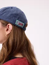 Gorra con visera curva de estilo clásico, confeccionada en algodón con efecto lavado. Presenta el logo de la marca Rusty bordado en el frente con letras en color rojo y borde blanco.