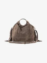 Cartera de mano confeccionada en cuero gamuzado color marrón, con diseño flexible y detalles de flecos laterales. Presenta un asa rígida metálica circular y una abertura superior fruncida.