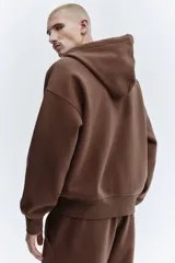 Campera con capucha H&M de corte oversized, confeccionada en tejido pesado de mezcla de algodón con interior cepillado. Presenta cierre frontal, hombros caídos, capucha forrada con cordón de ajuste y bolsillos tipo canguro. Puños y bajo acanalados.