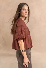 Blusa de viscosa y lino color crudo, con cuello en V, mangas tres cuartos abullonadas e inserciones de encaje floral y detalles plisados frontales.