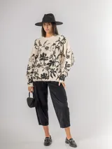 Sweater de punto con calce oversized, fondo color crudo y diseño estampado de flores en color negro. Presenta cuello redondo y mangas largas.