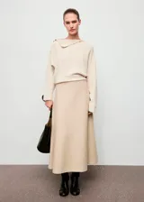 Jersey de punto color beige, con cuello asimétrico y detalle de botones efecto joya en el hombro, de manga larga y diseño recto.