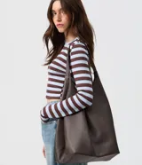 Cartera hobo grande de cuero marrón con acabado texturizado y diseño amplio, de estructura suave con asas integradas para el hombro y cierre interno con mosquetón.
