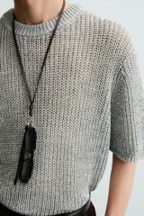 Camiseta de punto calado, color gris claro, de corte relajado (relaxed fit), con cuello redondo y mangas cortas.