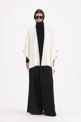 Spolverino abierto de corte amplio, color blanco con bordes en contraste de costura negra. Presenta un diseño envolvente tipo capa con mangas integradas.